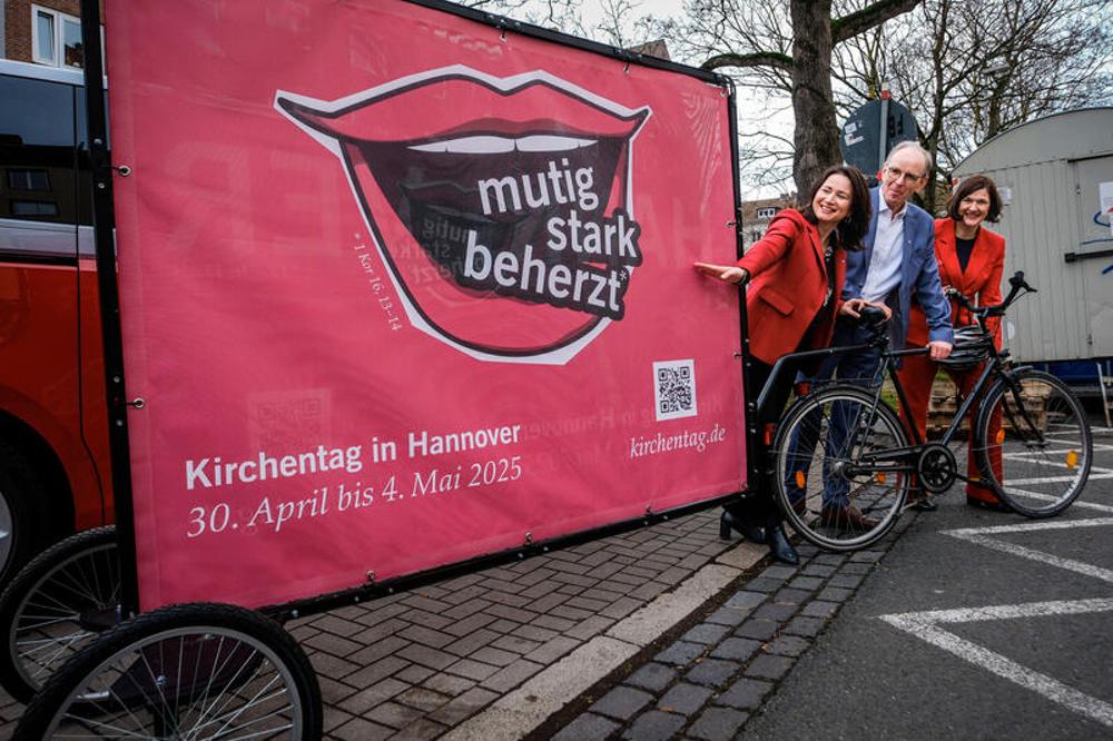 Anja Siegesmund, Ralf Meister und Kristin Jahn nebem einem Kirchentagsplakat