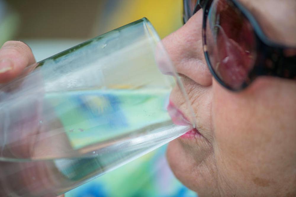 Eine &auml;ltere Frau trinkt an einem hei&szlig;en Sommertag ein Glas Wasser.